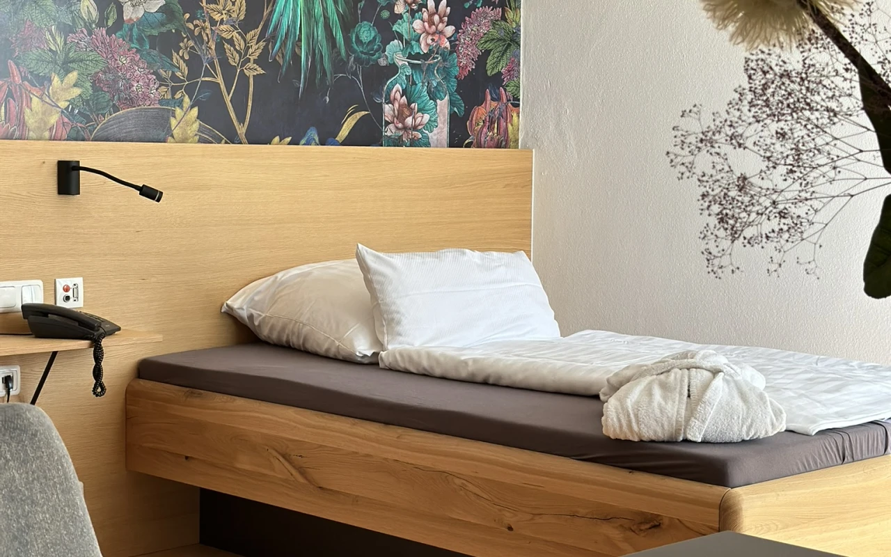 Bild Modernes Komfortzimmer mit Bett Schreibtisch, Sitzgelegenheit und dekorativer Wandgestaltung mit Vogelmotiv.
